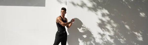 Uomo cubano muscoloso in occhiali e vestito nero guardando lontano mentre in piedi vicino all'edificio, striscione — Foto stock