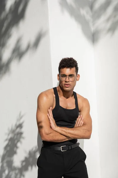 Jovem homem cubano muscular em óculos e sem mangas t-shirt cruzando braços e olhando para a câmera — Fotografia de Stock