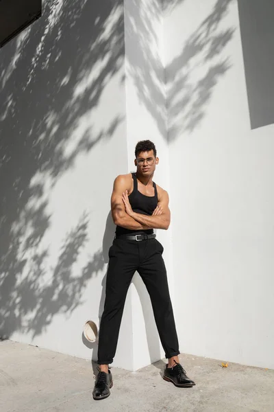 Piena lunghezza di fiducioso e muscoloso giovane cubano in occhiali da vista e vestito alla moda braccia incrociate — Foto stock