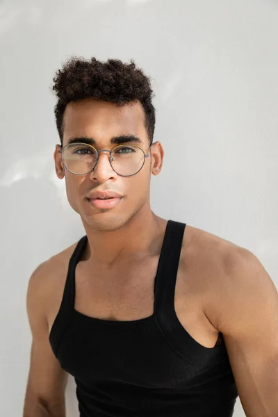 Portrait de jeune homme cubain bouclé dans des lunettes élégantes et t-shirt sans manches regardant la caméra — Photo de stock