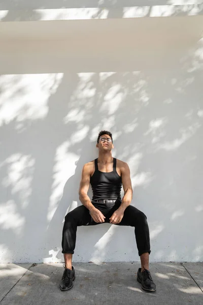 Relaxed young cuban man with closed eyes in eyeglasses and black outfit standing near wall — Stock Photo