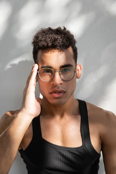 Ritratto di uomo cubano in t-shirt nera senza maniche che tocca gli occhiali alla moda e guarda la macchina fotografica — Foto stock