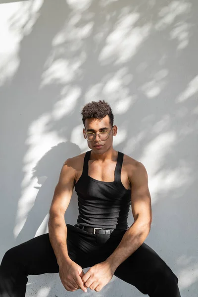 Расслабленный и стильный, мускулистый и молодой кубинский мужчина в черной одежде и очках — стоковое фото