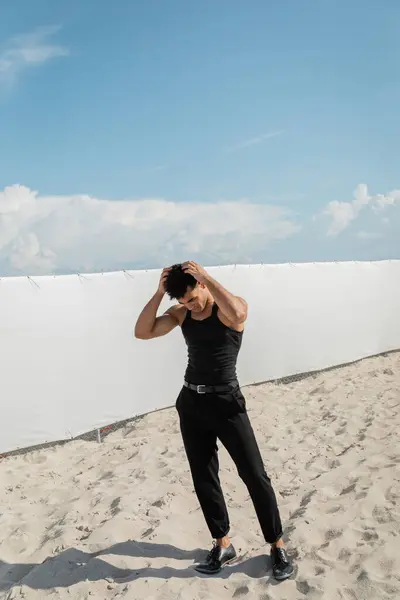 Uomo cubano in abito nero toccare i capelli mentre in piedi sulla sabbia sulla spiaggia di Miami — Foto stock