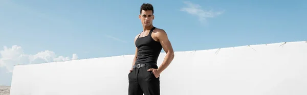 Muskulöser junger kubanischer Mann in schwarzer Kleidung posiert mit Händen in Taschen in Miami, Südstrand, Banner — Stockfoto