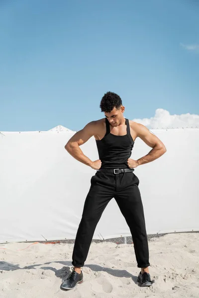 Élégant jeune homme cubain en noir t-shirt sans manches tenant la main sur les hanches à Miami, plage du sud — Photo de stock