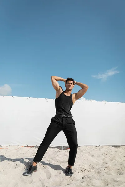 Homme fort et jeune cubain en tenue noire touchant la tête et regardant la caméra à Miami, plage du sud — Photo de stock