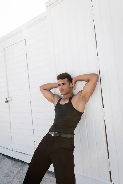 Moda e muscular jovem cubano homem relaxante e comovente cabeça enquanto está de pé ao ar livre — Fotografia de Stock