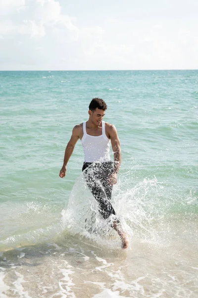 Улыбающийся и мускулистый молодой кубинский мужчина веселится, стоя в океанской воде на Майами Саут Бич — стоковое фото
