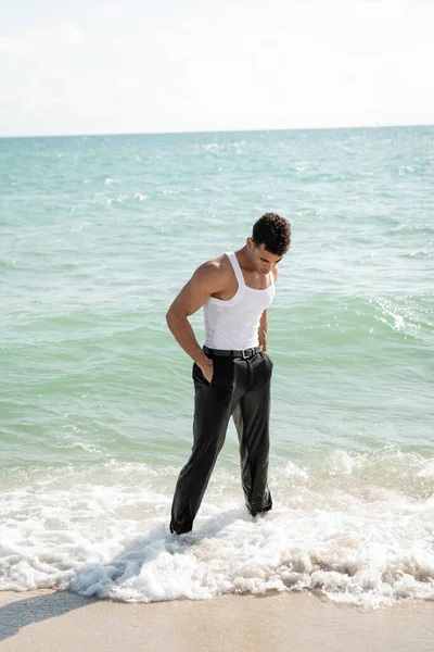 Kubaner in nasser Kleidung hält Hände in Taschen, während er im Ozeanwasser in Miami South Beach steht — Stockfoto
