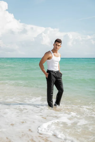 Jeune homme cubain musclé debout dans l'eau de l'océan à Miami South Beach, les mains dans les poches — Photo de stock