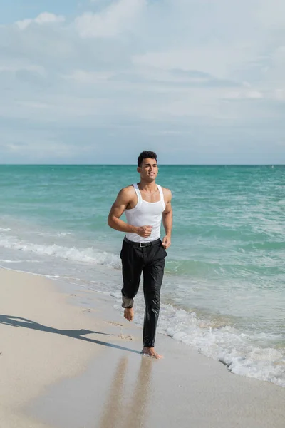 Muscular cuban young man running on sand near ocean water of Miami South Beach, Florida — Stock Photo