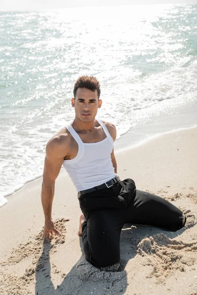 Gut aussehender und muskulöser kubanischer Mann, der in der Nähe des Ozeans in Miami South Beach posiert und in die Kamera blickt — Stockfoto