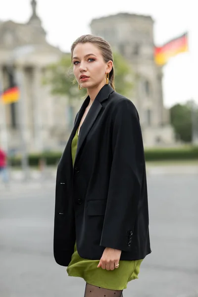 Porträt einer jungen blonden Frau in modischem Seidenkleid und schwarzer Jacke auf der Straße in Berlin — Stockfoto