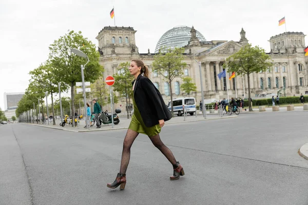 Voller Länge junge, hellhaarige Frau in Seidenkleid, Jacke und Stiefeln unterwegs in Berlin — Stockfoto