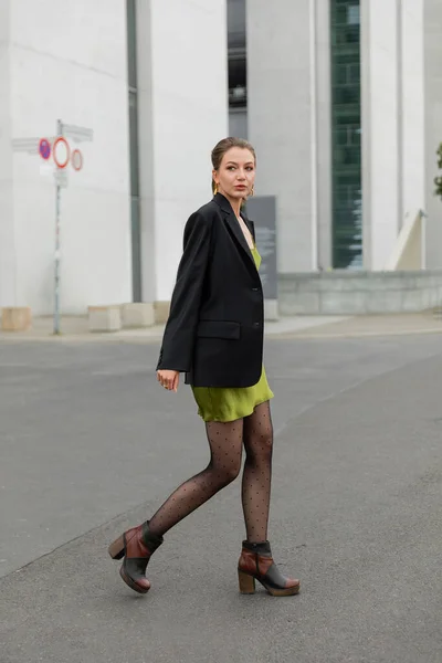 Jeune femme élégante en veste noire, robe en soie verte et collants modernes à Berlin — Photo de stock