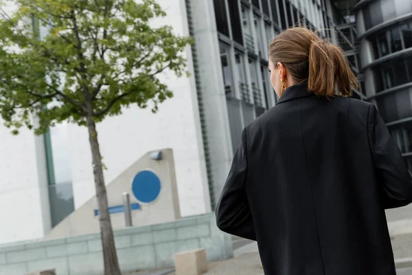 Vista posteriore di giovane donna dai capelli eleganti e biondi in giacca nera che cammina a Berlino, Germania — Foto stock