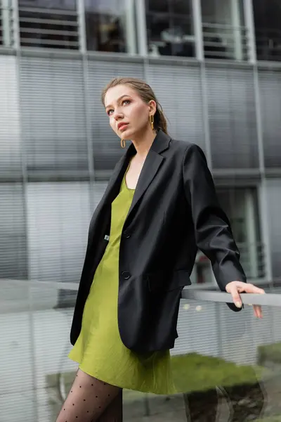 Fashionable fair haired woman in black blazer and silk dress standing near railing in Berlin — Stock Photo