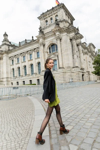 Trendige junge Frau in schwarzem Blazer, Seidenkleid und Stiefeln in Reichstagsnähe — Stockfoto