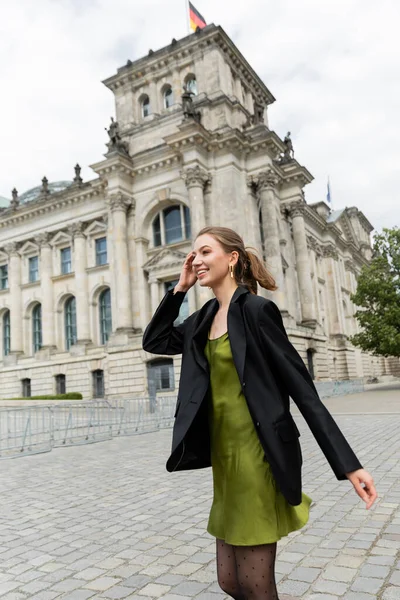 Giovane donna allegra ed elegante in giacca e abito di seta guardando lontano vicino al Reichstag Building — Foto stock