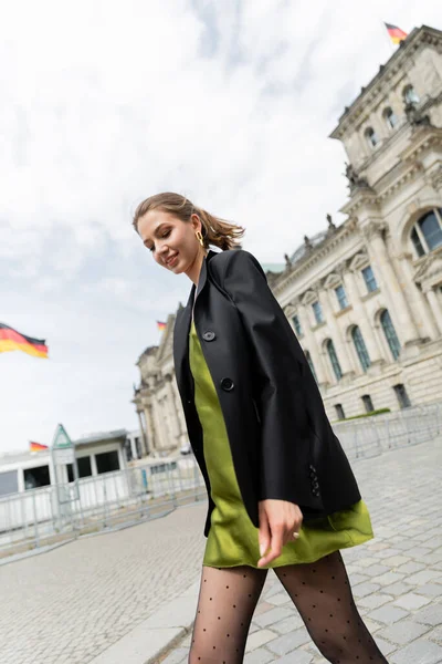 Fröhliche Frau in Blazer und grünem Seidenkleid spaziert in der Nähe des Reichstagsgebäudes in Berlin — Stockfoto