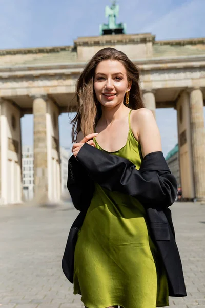 Ritratto di giovane donna in abito di seta e giacca che guarda la macchina fotografica vicino alla Porta di Brandeburgo — Foto stock