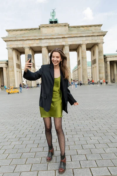 BERLÍN, ALEMANIA - 13 DE MAYO DE 2022: mujer feliz tomando selfie cerca de la Puerta de Brandeburgo en Berlín - foto de stock