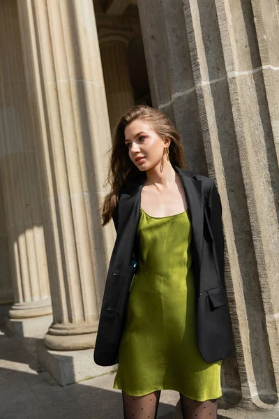 Elegant young fair haired woman in green silk dress and black jacket standing in Berlin — Stock Photo