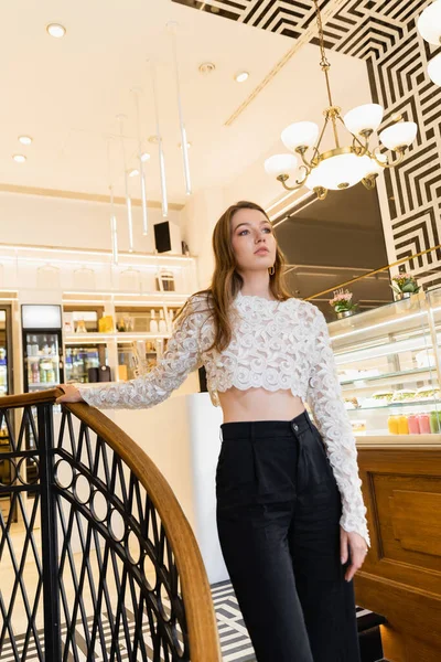 Молода і модна прекрасна волохата жінка в мереживному верху і штани, що стоять в сучасному кафе в Берліні — стокове фото