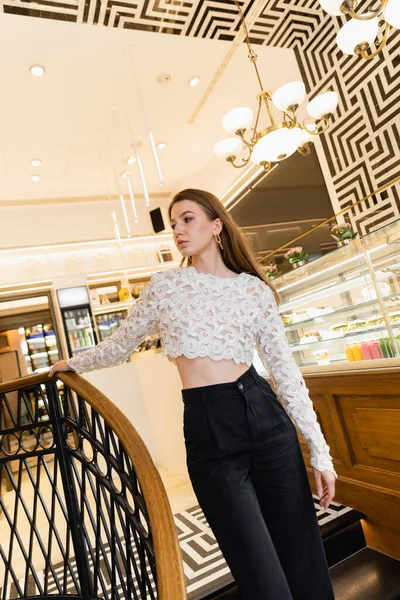 Fashionable young woman in lace top and pants standing near railing in cafe of Berlin, Germany — Stock Photo