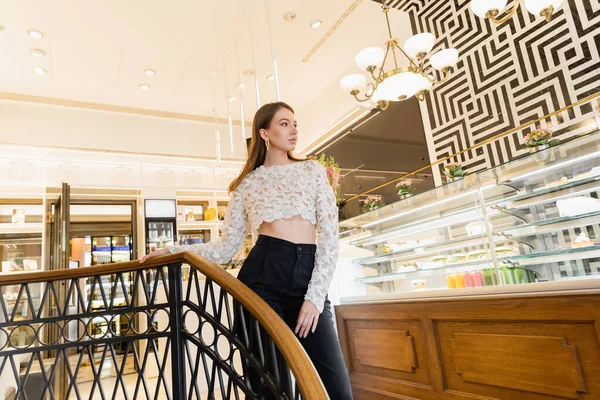 Selbstbewusste und junge blonde Frau in Spitzentop und Hose steht im Café — Stockfoto