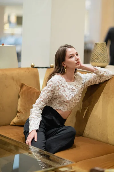 Entspannte blonde Frau in Spitzentop und Hose sitzt auf Sofa in Berliner Hotellobby — Stockfoto