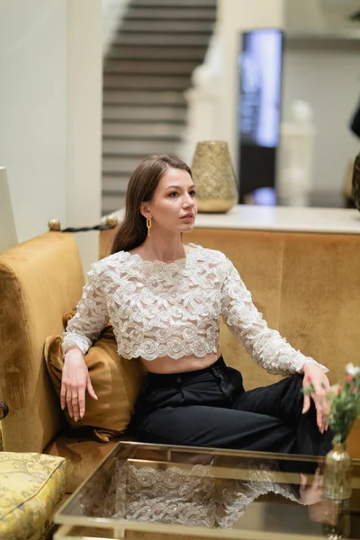 Модна прекрасна волохата жінка в мереживній верхній частині і штани, що сидять на дивані в готельному лобі Берліна — стокове фото