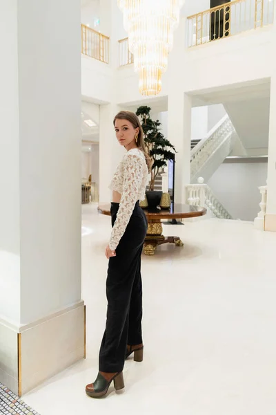 Modische Frau in Spitzentop, Hose und Stiefeln in voller Länge blickt in Berliner Hotel in die Kamera — Stockfoto