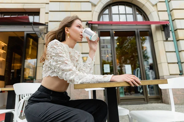 Junge und modische blondhaarige Frau im Spitzentop trinkt Kaffee aus Pappbecher — Stockfoto