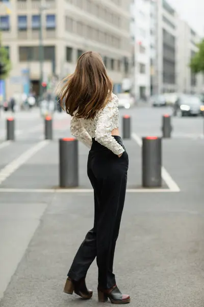 Visão traseira da jovem mulher de cabelos bonitos em top de renda e calças de cintura alta em pé na rua em Berlim — Fotografia de Stock