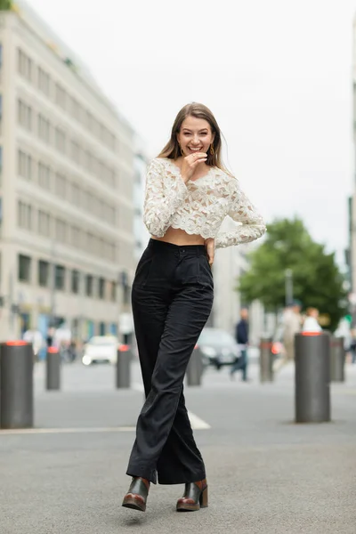 Happy young woman posing in lace top and high waist pants standing on street in Berlin — Stock Photo