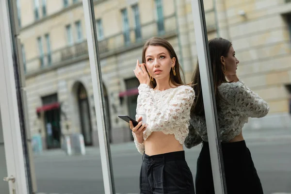 Giovane donna pensierosa che tiene lo smartphone mentre si trova vicino all'edificio in strada a Berlino, Germania — Foto stock