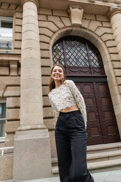 Щаслива молода жінка в мереживній верхній і високій талії штани, дивлячись на камеру на міській вулиці в Берліні — стокове фото