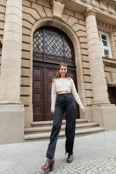 Весела молода жінка в мереживній верхній і високій талії штани дивиться на камеру на міській вулиці в Берліні — стокове фото