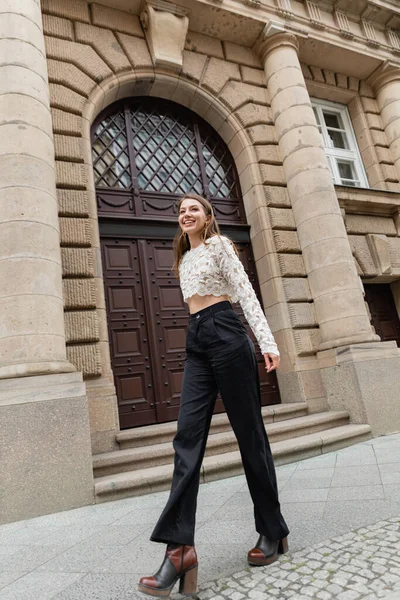 Piacere giovane donna in pizzo e pantaloni a vita alta guardando la fotocamera sulla strada urbana di Berlino — Foto stock