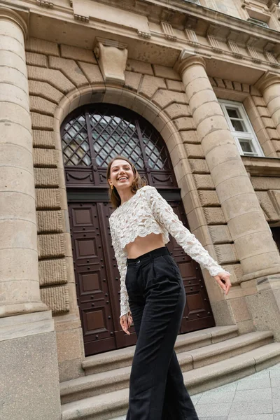 Оптимістична молода жінка в мереживній верхній і високій талії штани дивиться на камеру на міській вулиці в Берліні — стокове фото