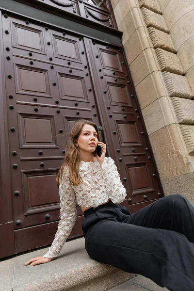 Young woman talking on smartphone while sitting on stairs near entrance of building in Berlin — Stock Photo