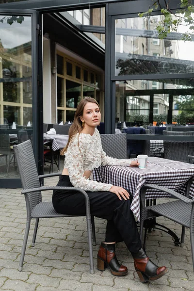 Молодая женщина сидит с бумажной чашкой на террасе открытого кафе и городской улице в Берлине — стоковое фото