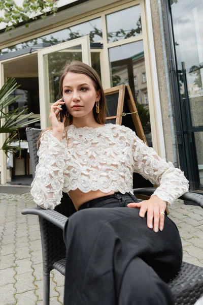 Стильная женщина разговаривает по смартфону во время отдыха на террасе кафе на улице в Берлине — стоковое фото