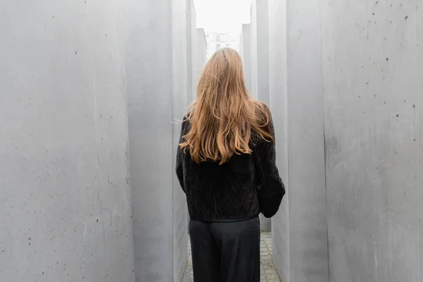Vista posterior de la mujer en chaqueta negra caminando entre piedras de Memorial to Murdered Jews of Europe - foto de stock