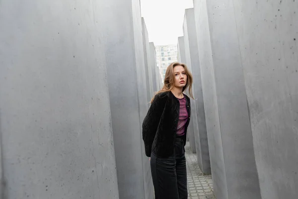 Eine blonde junge Frau in Jacke steht zwischen dem Denkmal für die ermordeten Juden Europas in Berlin — Stockfoto