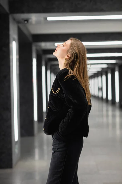 Trendige junge Frau in schwarzer Jacke posiert in modernem Gebäude mit Leuchtstoffröhren in Berlin — Stockfoto