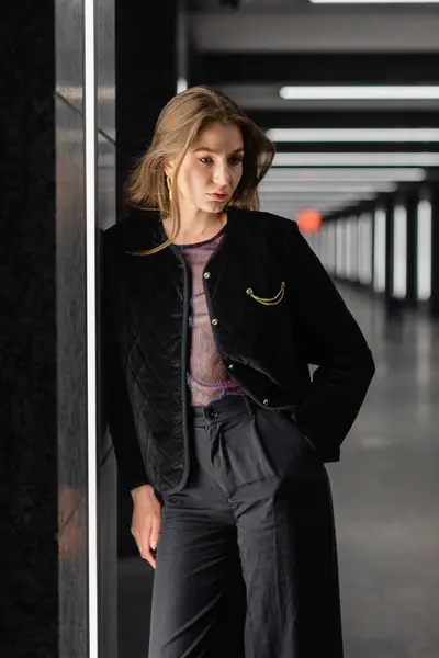 Hübsche junge Frau in schwarzer Jacke posiert in modernem Gebäude mit Leuchtstoffröhren in Berlin — Stockfoto