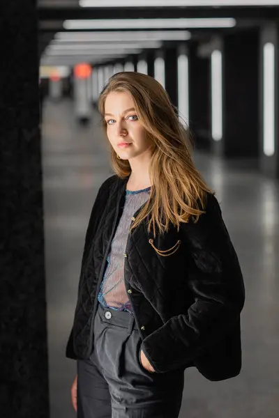 Attraktive junge Frau in schwarzer Jacke posiert in modernem Gebäude mit Leuchtstoffröhren in Berlin — Stockfoto